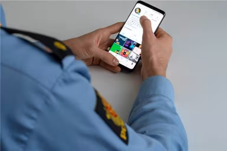 Bildet over skulderen til en politimann som sitter med en mobiltelefon med referanse til nettpatruljen.