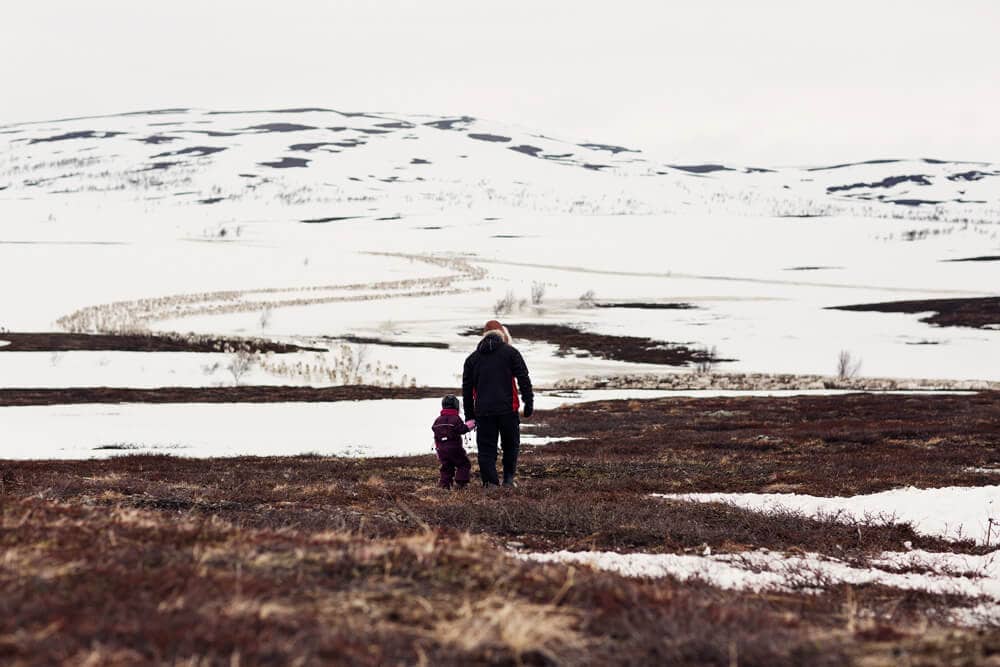 Bildet viser en vidde, med en samisk mann som holder sitt barn i hånden omgitt av viddenaturen.