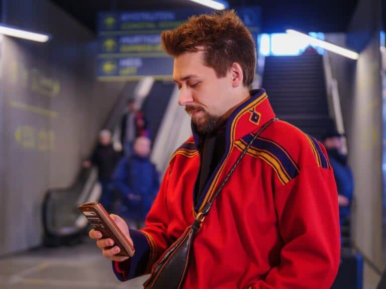 En ung samisk mann i kofte sjekker mobiltelefonen sin i en reisesituasjon.