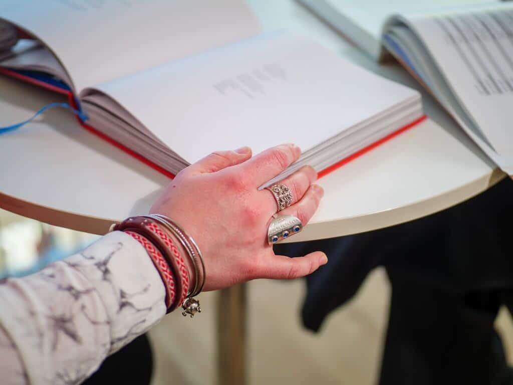 Bilde av en kvinnehånd med samiske ringer og armbånd, som blar i en bok.